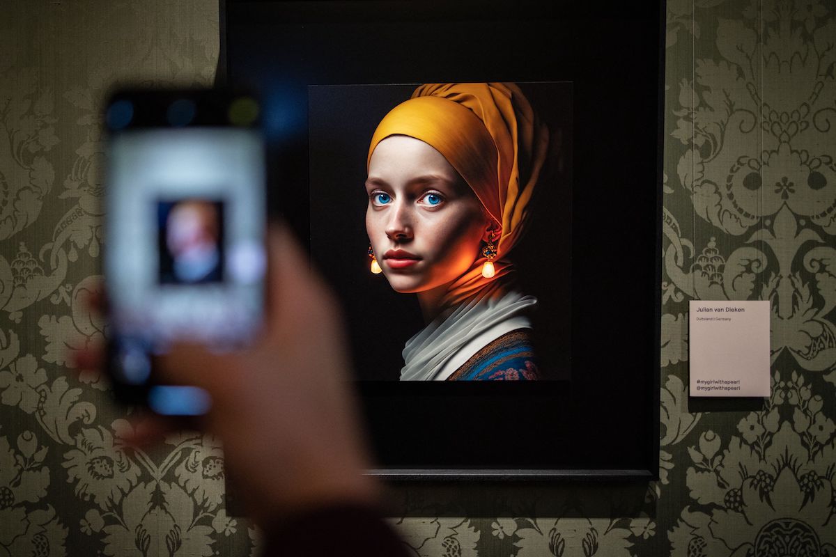 A visitor takes a picture with his mobile phone of an image designed with artificial intelligence by Berlin-based digital creator Julian van Dieken (C) inspired by Johannes Vermeer's painting "Girl with a Pearl Earring" at the Mauritshuis museum in The Hague