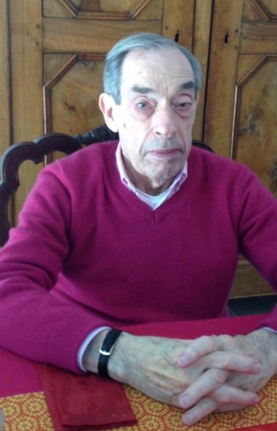 An elderly man in a purple jumper sitting at a dining table